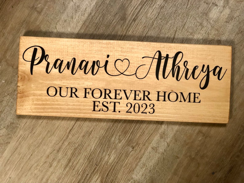 May include: A wooden sign with the text "Pranavi & Athreya Our Forever Home Est. 2023" in black lettering.