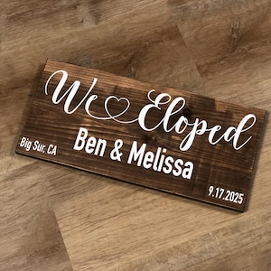 May include: A rectangular wooden sign with the words "We Eloped" in white script, along with the names "Ben & Melissa" and the date "9.17.2025". The sign also includes "Big Sur, CA".