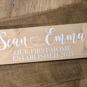 May include: A wooden sign with the text "Sean & Emma Our First Home Established 2023" in white lettering.