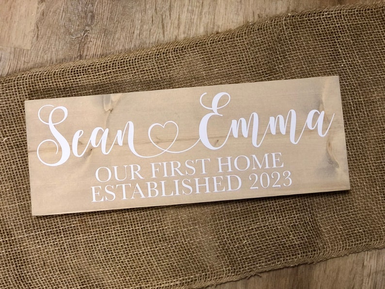 May include: A wooden sign with the text "Sean & Emma Our First Home Established 2023" in white lettering.