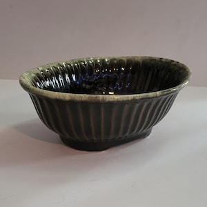 May include: A dark green and cream glazed ceramic bowl with a fluted design. The bowl is oval shaped and has a glossy finish.