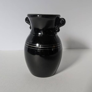 May include: A black glass vase with silver trim and two handles. The vase has a rounded body and a flared top.