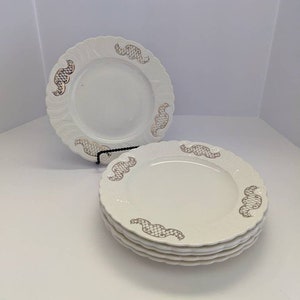 May include: Set of four white ceramic dinner plates with a gold, intricate design around the rim.