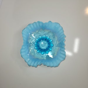 May include: A light blue glass bowl with a ruffled edge and a blue and white grape design. The bowl has a scalloped edge and a raised center.