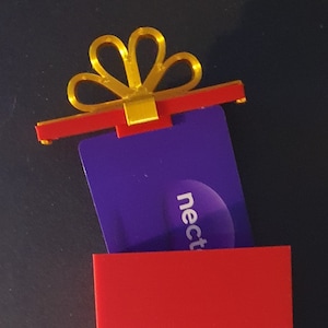 May include: A red gift box with a gold bow and a purple gift card inside. The gift card has the word "nect" printed on it.