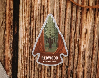 May include: A sticker with a red arrow design featuring a green forest scene. The sticker says "Redwood National Park" in white text.