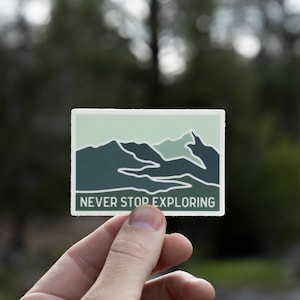 May include: A sticker with a green and blue mountain range design and the text "NEVER STOP EXPLORING".