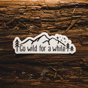 May include: White sticker with a black mountain range, trees, and stars. The text "Go wild for a while" is written below the mountains.