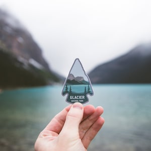 May include: A gray arrow-shaped sticker with a mountain scene and the text "Glacier National Park".
