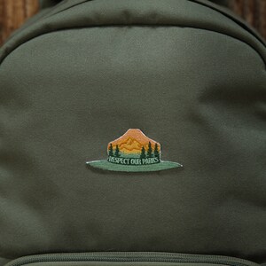 Park Ranger Hat Patch. Green, Orange and yellow patch in the shape of a ranger hat with mountains, trees and the words "respect our parks"