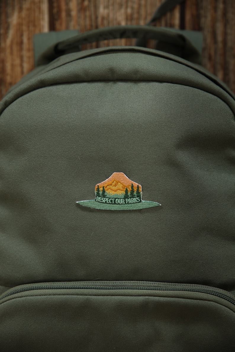 Park Ranger Hat Patch. Green, Orange and yellow patch in the shape of a ranger hat with mountains, trees and the words "respect our parks"