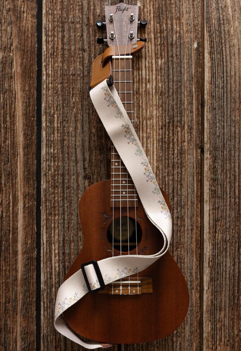 Cute tan floral strap printed with Little colored flowers across the length of the strap attached to Ukulele lying on wood floor