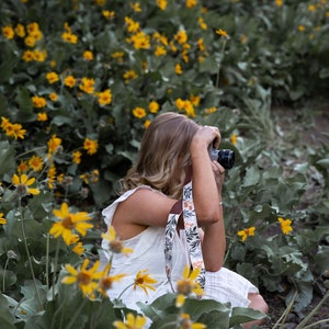 women sitting in flowers taking photos with camera and floral camera strap