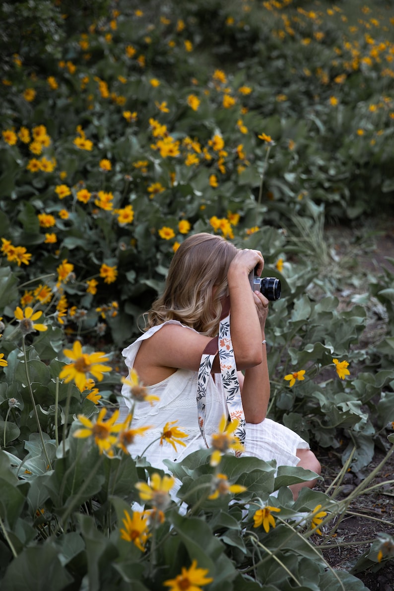 women sitting in flowers taking photos with camera and floral camera strap