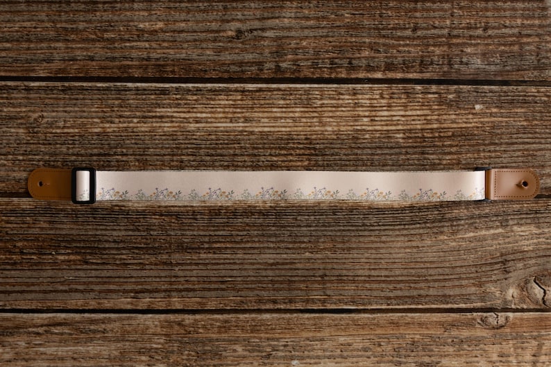 Cute tan floral strap printed with Little colored flowers across the length of the strap lying on wood floor