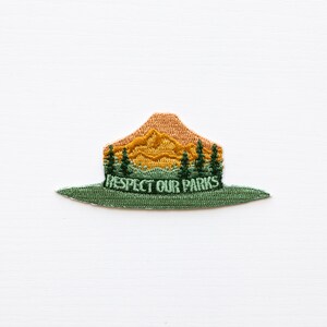 Park Ranger Hat Patch. Green, Orange and yellow patch in the shape of a ranger hat with mountains, trees and the words "respect our parks"