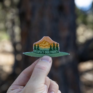 park ranger hat patch held up by hand in front of tree