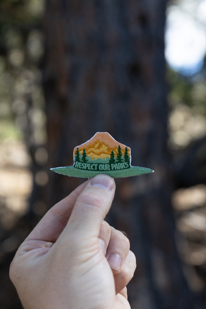 park ranger hat patch held up by hand in front of tree