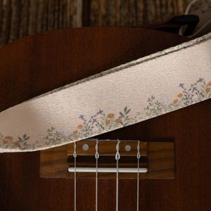 Cute tan floral strap printed with Little colored flowers across the length of the strap attached to Ukulele lying on wood floor