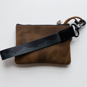 midnight mountain black keychain. Printed with mountains and stars. Attached to brown leather wallet