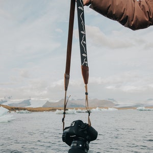 women holding out simple mountain design camera strap connected to camera