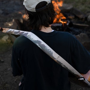 man sitting at campfire playing guitar wearing national park guitar strap in Color features 18 National Park illustrations printed along the length of the strap. Brown leather ends.