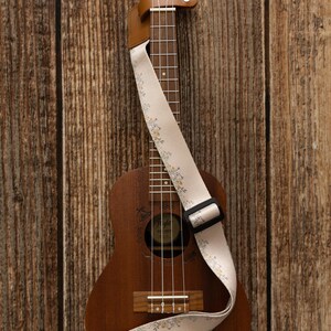 Cute tan floral strap printed with Little colored flowers across the length of the strap attached to Ukulele lying on wood floor