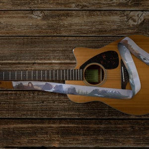 national park guitar strap attached to acoustic guitar lying on wood floor