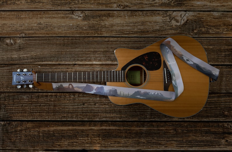 national park guitar strap attached to acoustic guitar lying on wood floor