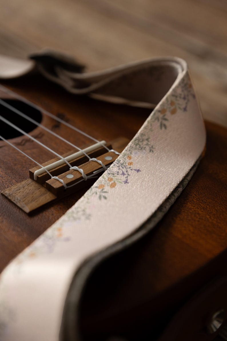 Cute tan floral strap printed with Little colored flowers across the length of the strap attached to Ukulele lying on wood floor