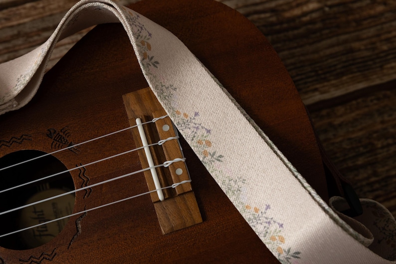 Cute tan floral strap printed with Little colored flowers across the length of the strap attached to Ukulele lying on wood floor