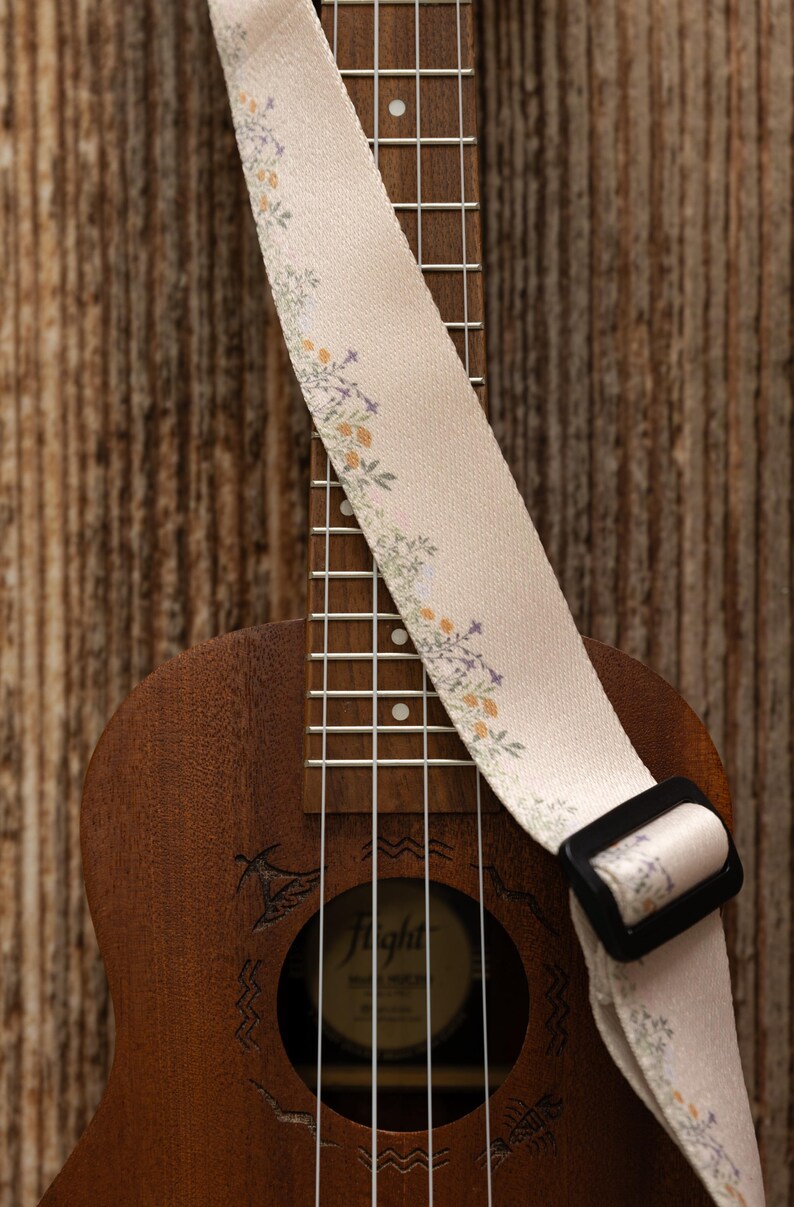 Cute tan floral strap printed with Little colored flowers across the length of the strap attached to Ukulele lying on wood floor