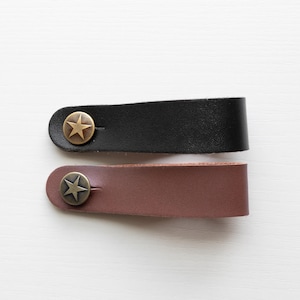 May include: Two leather straps with a star-shaped metal buckle. The strap on top is black and the strap on the bottom is brown.