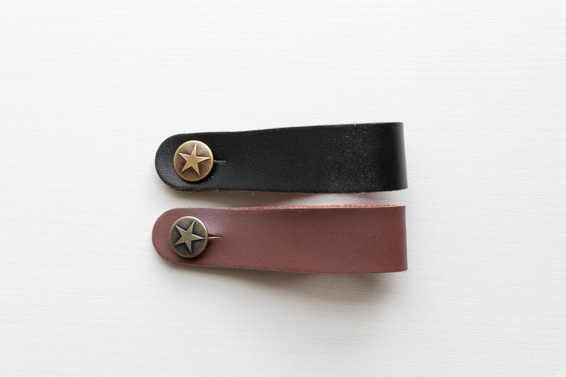 May include: Two leather straps with a star-shaped metal buckle. The strap on top is black and the strap on the bottom is brown.