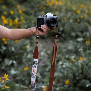 women holding out camera with wildflower camera strap dangling