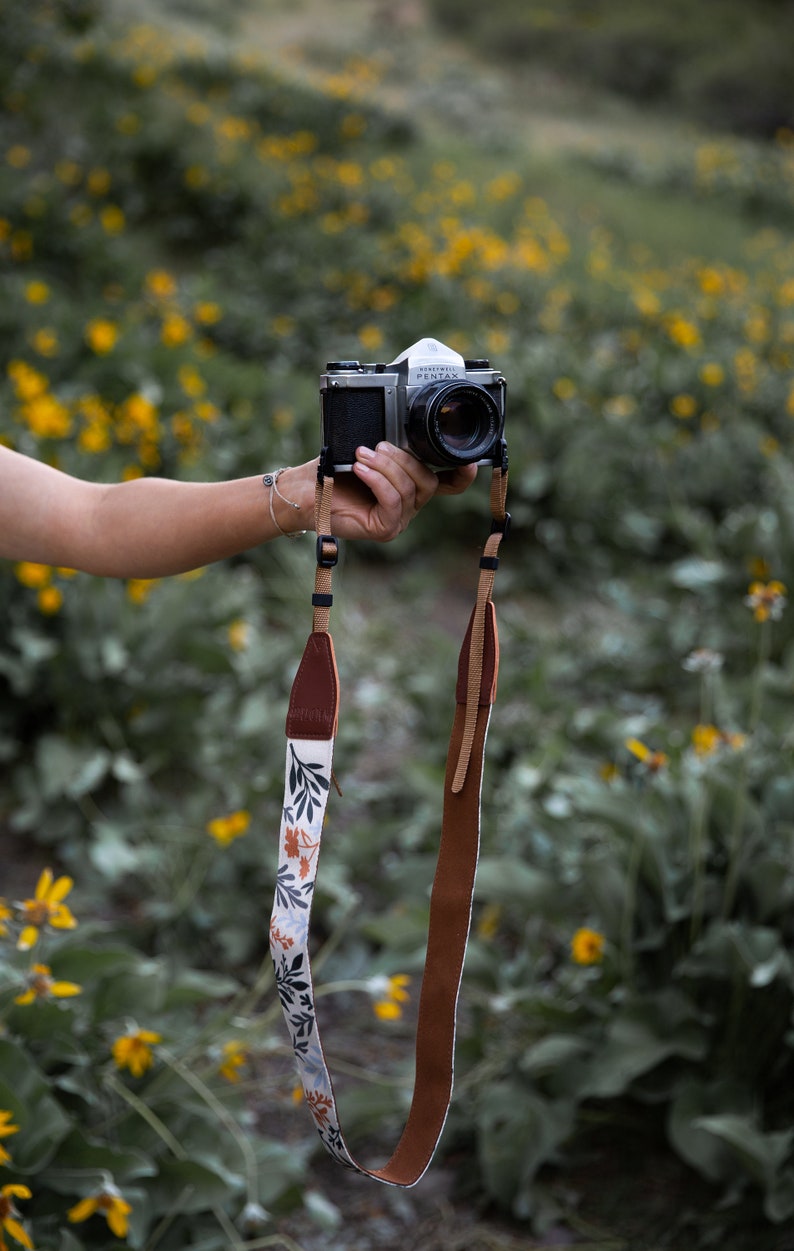 women holding out camera with wildflower camera strap dangling