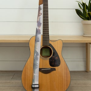 national park guitar strap attached to acoustic guitar lying against wood bench