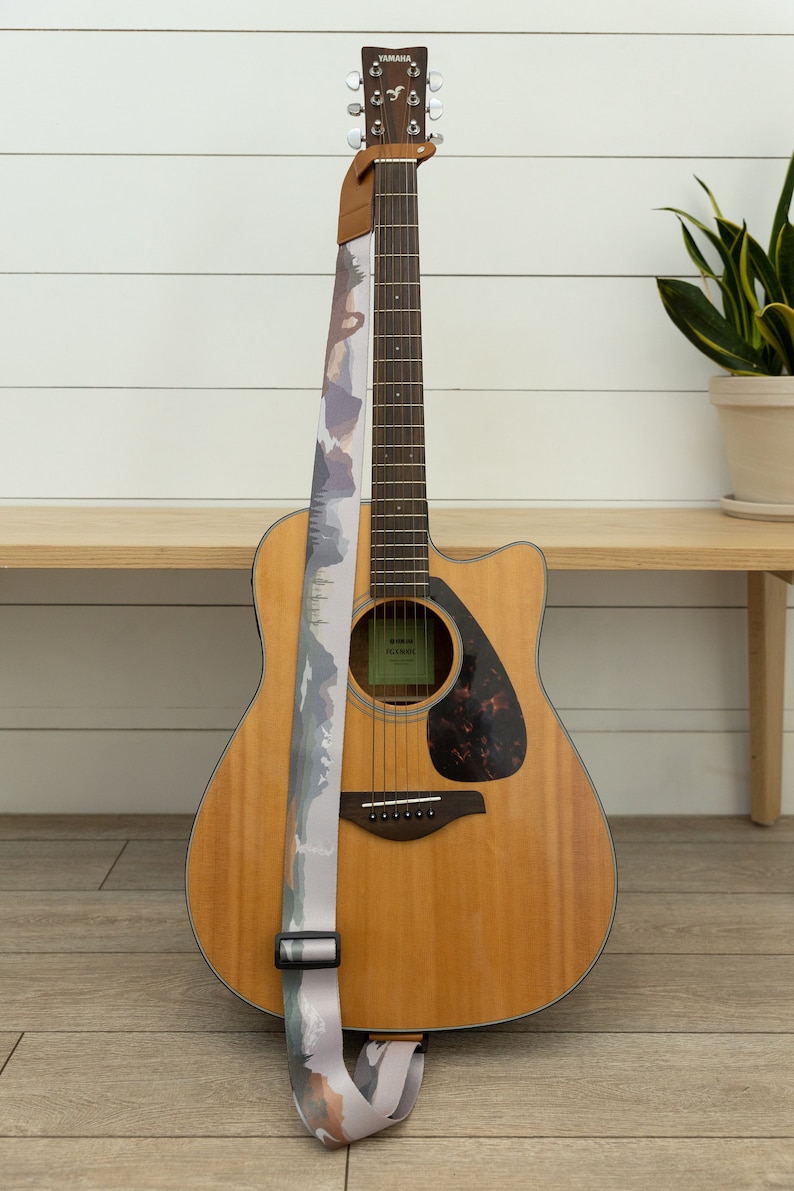 national park guitar strap attached to acoustic guitar lying against wood bench