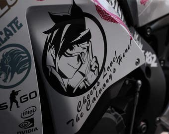 May include: A close-up of a motorcycle with various decals. The primary decal features a black and white anime-style character with the text "Cheers Love! The Calvary's Here!" Other decals include logos and text.