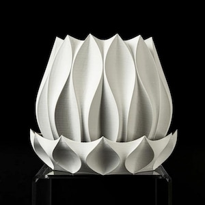 May include: A white ceramic planter with a unique, folded design resembling a flower. The planter has a wide, open top and a smaller, decorative base.