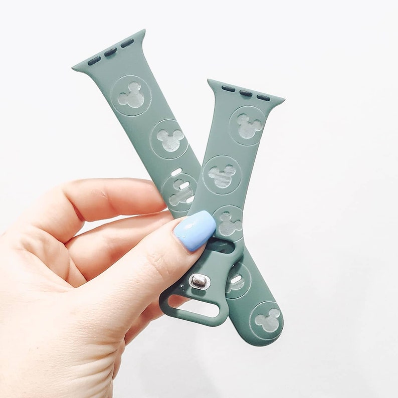 May include: Two green silicone Apple Watch bands with a white Mickey Mouse silhouette pattern.