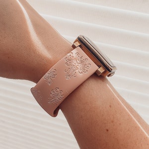 May include: A pink silicone watch band with a gold watch face and a floral pattern.