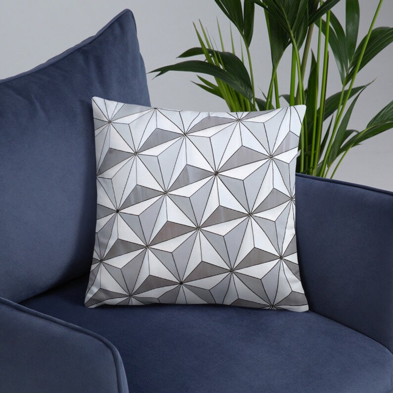 K&ouml;nnte beinhalten: Ein wei&szlig;es Kissen mit einem geometrischen Muster aus grauen und wei&szlig;en Dreiecken. Das Kissen liegt auf einem blauen Sofa.