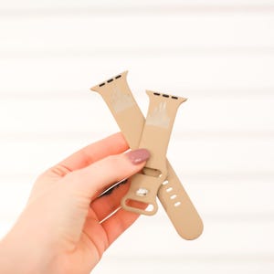 May include: Two beige silicone Apple Watch bands with a white castle design. The bands are crossed over each other.