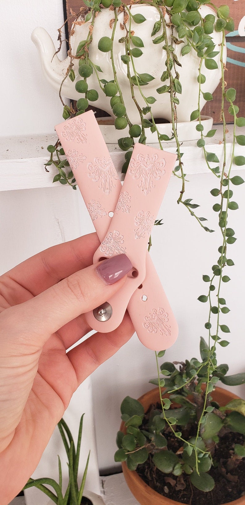 May include: Two pink silicone watch bands with a white floral pattern. The bands have a silver metal button.