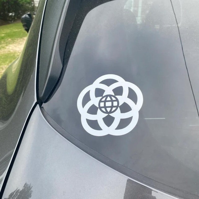 May include: White vinyl sticker of the Epcot logo, a stylized flower with a globe in the center, on a gray car window.