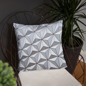 K&ouml;nnte beinhalten: Ein wei&szlig;es Kissen mit einem geometrischen Muster aus grauen Dreiecken. Das Kissen liegt auf einem Stuhl mit einem Metallgestell.