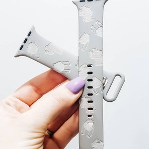 May include: A gray Apple Watch band with a white design of small animals. The band is made of silicone and has a textured surface.