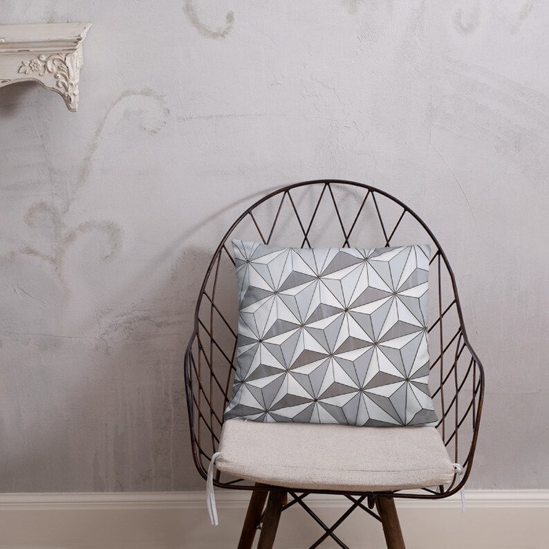 K&ouml;nnte beinhalten: Ein graues und wei&szlig;es Kissen mit geometrischem Muster auf einem Metallstuhl. Das Kissen hat ein modernes Design mit einem sich wiederholenden Muster aus Dreiecken.