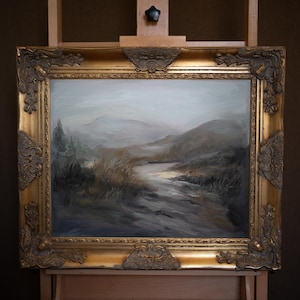 May include: An oil painting of a landscape scene, framed in a gold ornate frame. The artwork depicts a river winding through a valley, with mountains in the background. The color palette is muted, with shades of gray, brown, and green.
